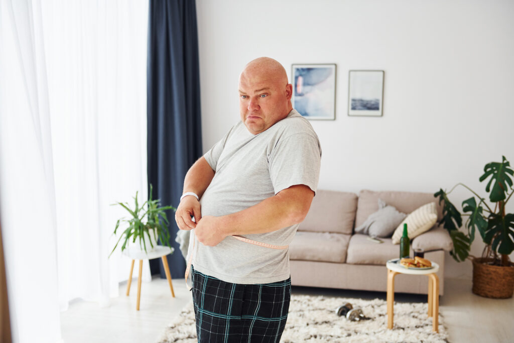 A Man Measuring His Waist In Front Of The Mirror Looking Sad, Considering Whether His Weight And Erectile Dysfunction Are Connected