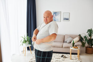 a man measuring his waist in front of the mirror looking sad, considering whether his weight and erectile dysfunction are connected