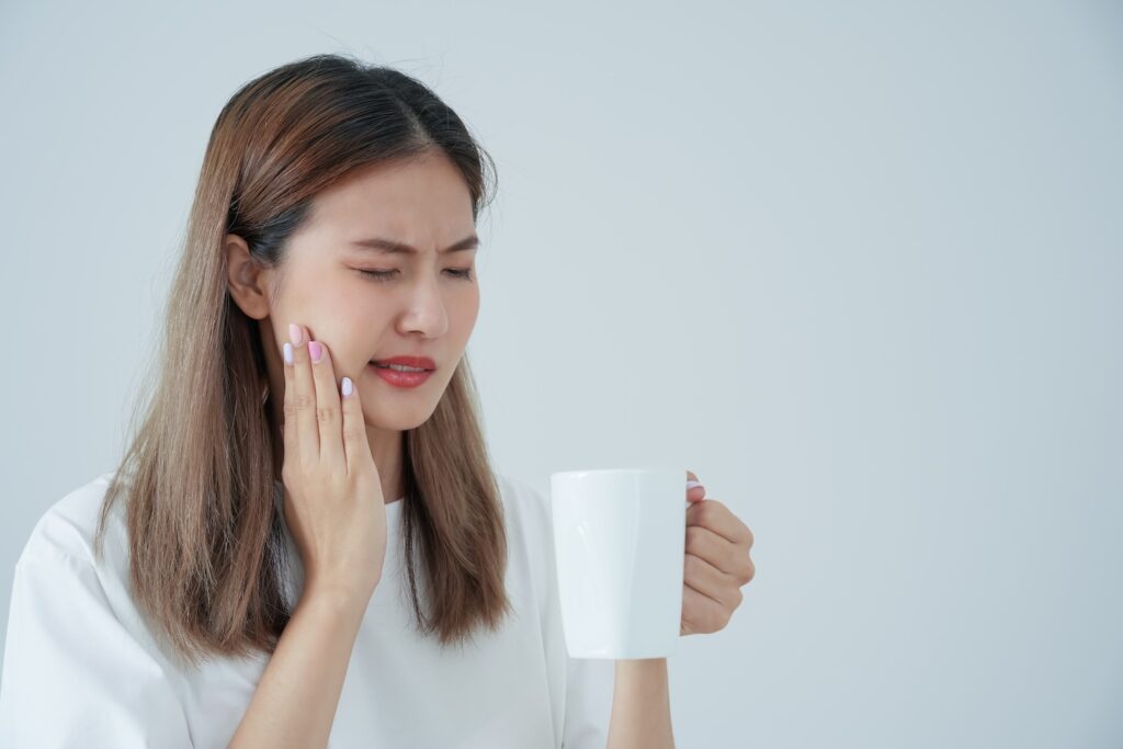 A woman drinking a hot drink and experiencing tooth sensitivity. She has read the Colgate Duraphat reviews from Real Users and feels reassured she could relieve this tooth pain by using Colgate Duraphat.