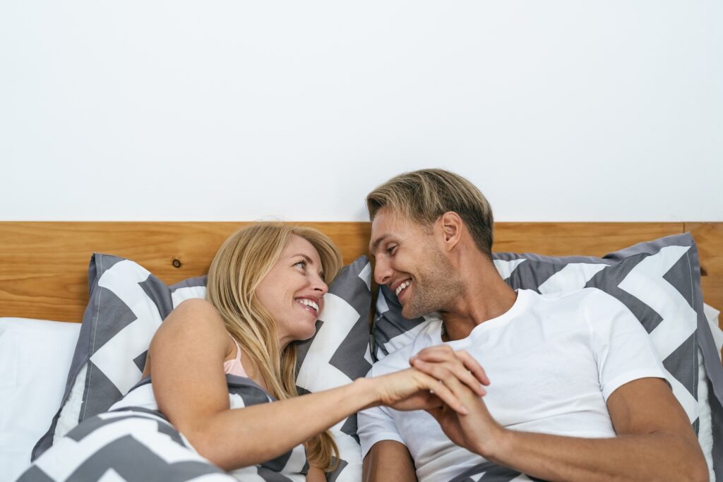 Happy smiling couple lying on bed having tender moments after learning how to treat erectile dysfunction