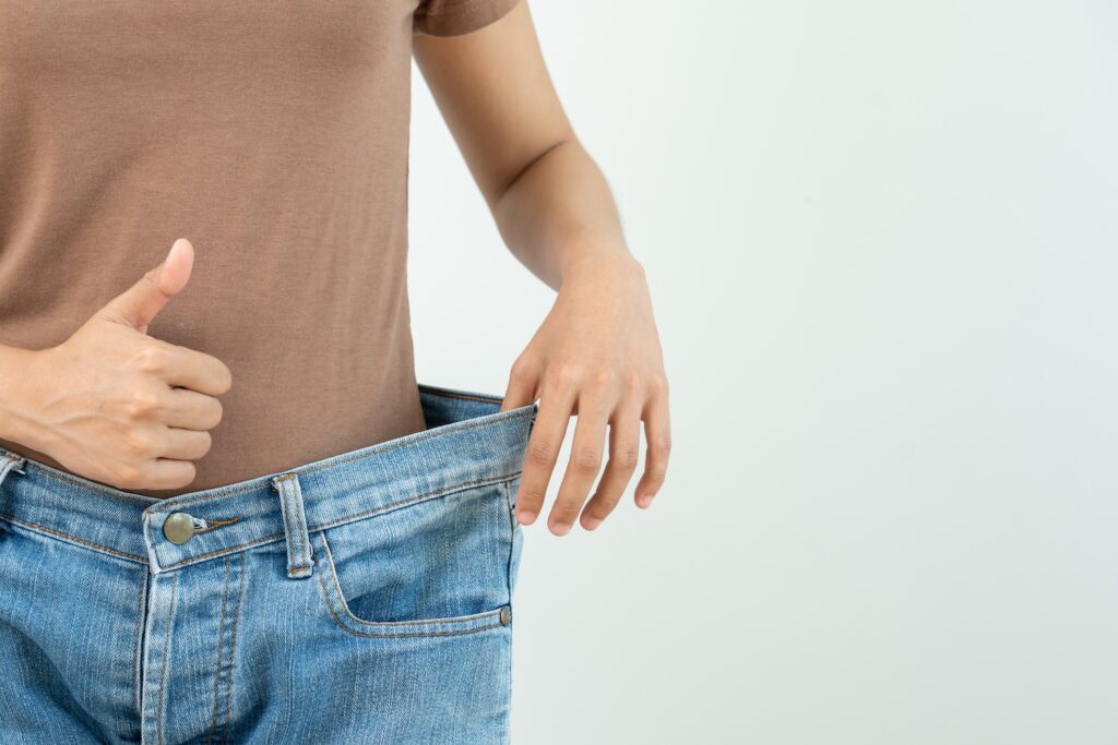 A woman holding open her trousers showing she has lost weight. She answering 'is mounjaro effective for weight loss' with a thumbs up