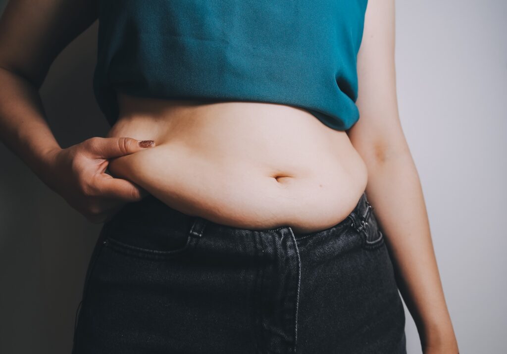 a woman holding her belly deciding the difference between fat dissolving injections vs weight loss injections