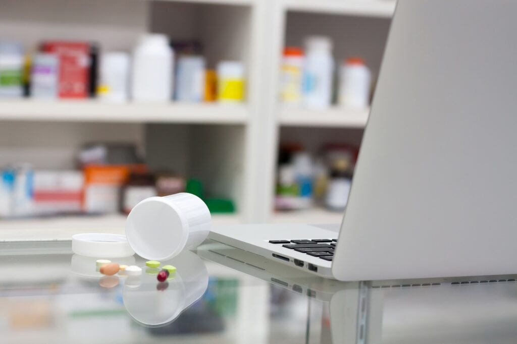 an image of a laptop on a desk, with a bottle of tablets, in a pharmacy, showing how online pharmacies work