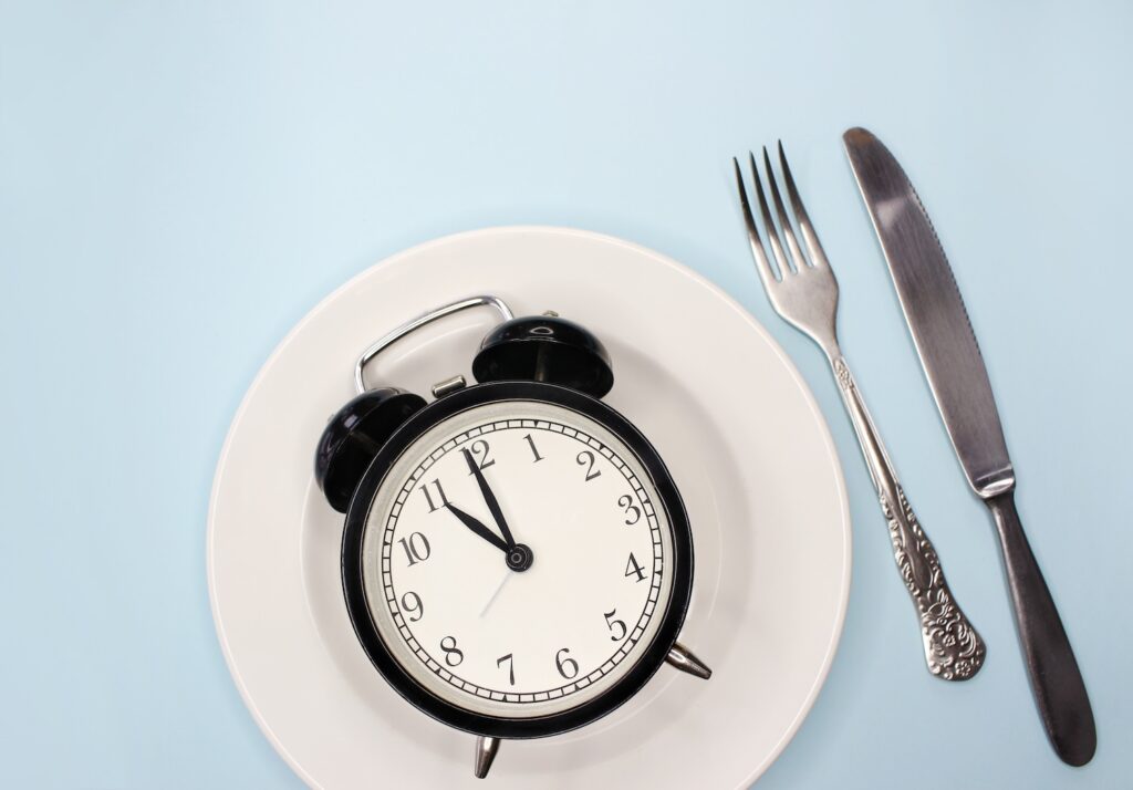 An alarm clock on an empty plate, next to a knife and fork to express if you can fast on mounjaro or wegovy