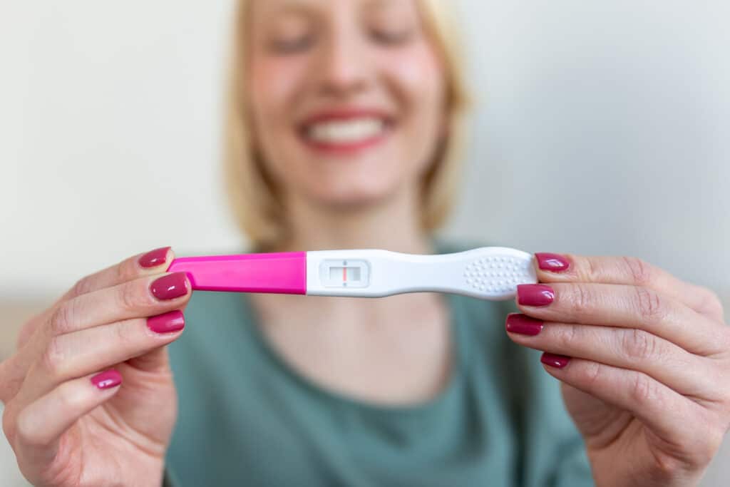 A woman holding a pregnancy testing and smiling because she asked 'Can Mounjaro affect fertility'