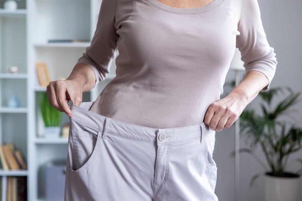 A woman showing weight loss achievement by holding oversized trousers, wondering what is CagriSema