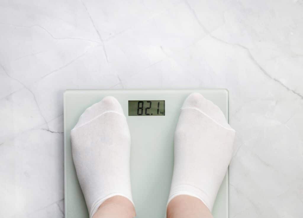 Feet in white socks standing on scales, considering the difference between nevolat vs Mounjaro for weight loss