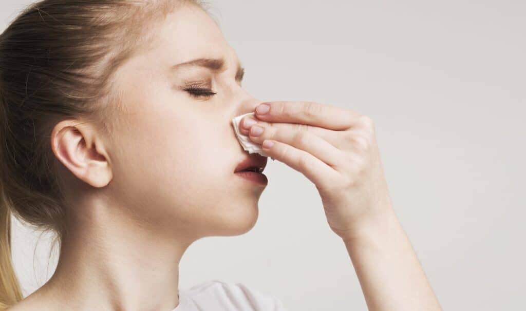 Young woman blowing her nose to represent how to clear a clogged nose